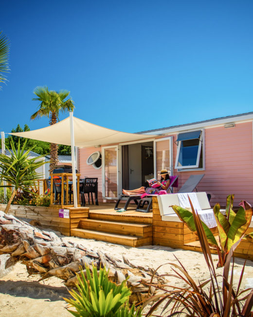 Camping Californie Plage - Locations - Hébergement avec terrasse semi couverte entouré de palmiers